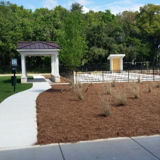 A landscaped park area featuring a pathway leading to a gazebo, surrounded by greenery and trees.