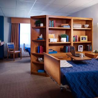A cozy and organized interior space featuring a desk, shelves, and a neatly made bed.