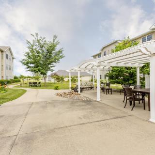 A peaceful outdoor space featuring a pergola with seating, surrounded by greenery and apartment buildings.