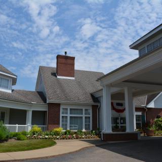 A residential building with a covered entrance and landscaped surroundings under a partly cloudy sky.