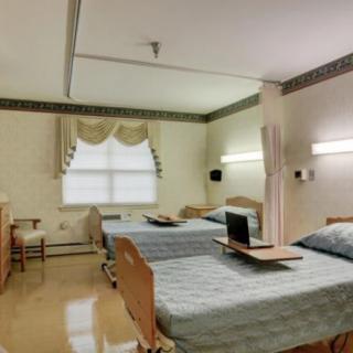 A clean and well-organized hospital room featuring two patient beds with trays, a window with curtains, and ambient lighting.