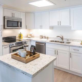 A modern kitchen featuring white cabinets, stainless steel appliances, and a central island with a marble countertop.