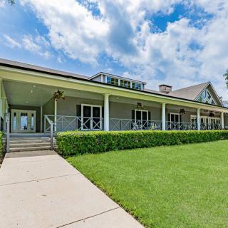 A beautiful house with a wide porch and lush green lawn under a partly cloudy sky.