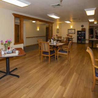 A cozy dining area with wooden flooring, neatly arranged tables and chairs, ambient lighting, and decorative flowers on the tables.