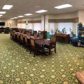 A spacious dining or conference room with a long table surrounded by chairs, featuring a patterned carpet and several windows.