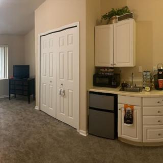 A cozy living area featuring a kitchenette with a mini fridge and storage cabinets, alongside a TV and closet.