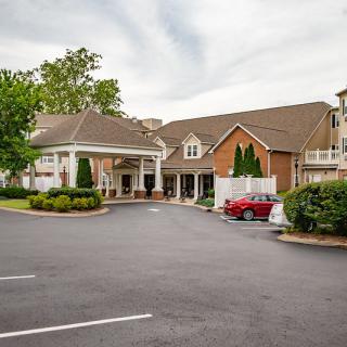 A view of a building with a parking lot and surrounding greenery on a cloudy day.
