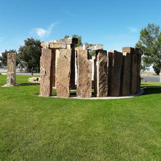 A stone circle sculpture set on a lush green lawn under a clear blue sky.