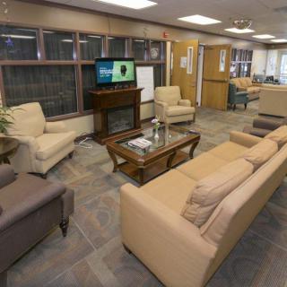 A comfortable lounge area featuring sofas, armchairs, a coffee table, and a television, with bookshelves lining the wall.
