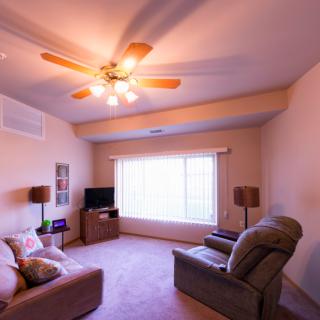 A cozy living room with a sofa, recliner, TV, and ceiling fan.