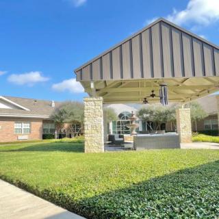 A well-maintained outdoor pavilion surrounded by a lush green lawn under a clear blue sky.