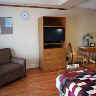 A cozy room featuring a sofa, a bed with a patterned blanket, a television unit, and a small dining table.