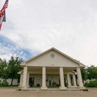 A building with columns and a flagpole against a cloudy sky.