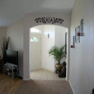 A cozy living room with an archway leading to the entryway, decorated with a potted plant and wall art.