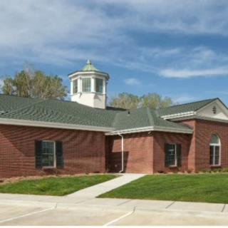 A brick building with a green roof and cupola, surrounded by a well-kept lawn.