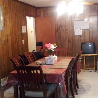 A cozy dining room with wood paneling, featuring a dining table set for eight and a small television in the corner.
