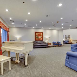 A spacious lounge area with a white piano, various seating options, and soft lighting.