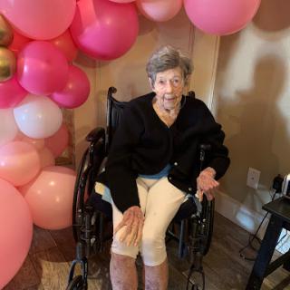 An elderly woman in a wheelchair surrounded by colorful balloons.