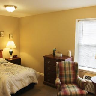 A cozy bedroom with a bed, dresser, and an armchair near a window.