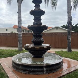 A multi-tiered fountain surrounded by palm trees in a garden setting.