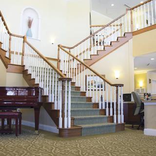 A grand staircase in a well-lit lobby, with a piano nearby and elegant interior design elements.