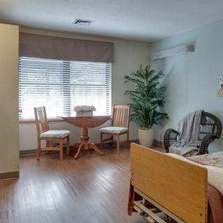 A cozy room with a small table and chairs, a bed, and a potted plant near the window.