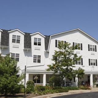 A large white residential building with surrounding greenery under a clear blue sky.