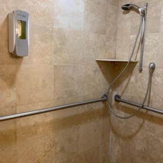 A tiled bathroom shower with a grab bar, soap dispenser, and adjustable shower head.