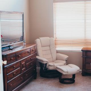A cozy corner of a living room featuring a recliner chair, dresser, and natural light.