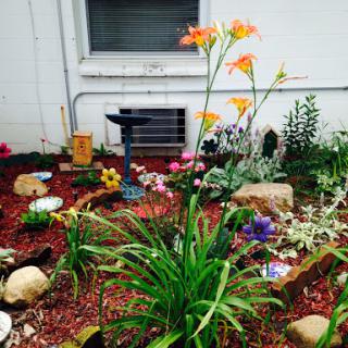 A vibrant garden featuring blooming flowers, colorful stones, and a serene birdbath.