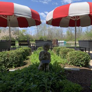 A pleasant outdoor patio with red and white umbrellas, surrounded by greenery and a small statue.