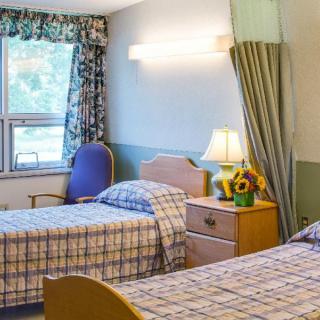 A cozy bedroom with two single beds, a window with curtains, and a nightstand holding a lamp and flowers.