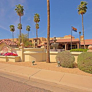 A desert-style building with palm trees and a flag on a clear day.