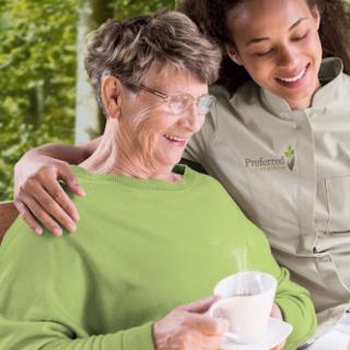 A caregiver shares a joyful moment with an elderly woman, enjoying a cup of tea in a serene outdoor setting.