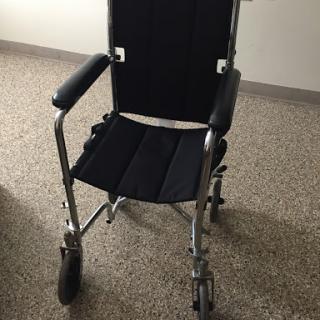 A black wheelchair with a metal frame, designed to assist individuals in mobility.