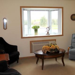 A cozy living room with a large bay window, comfortable chairs, and a wooden coffee table adorned with flowers.