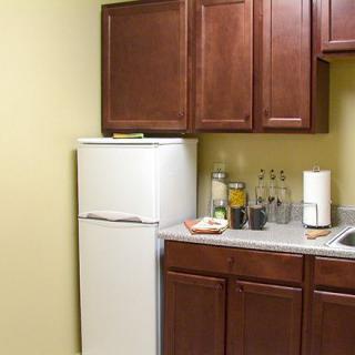 A small kitchen area featuring a white refrigerator, wooden cabinets, bottles on the countertop, and a sink.