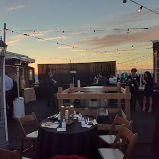 An elegant outdoor gathering on a rooftop, featuring beautifully set tables against a stunning sunset backdrop.
