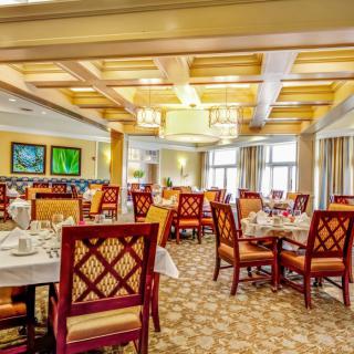 An elegant dining room with neatly arranged tables and chairs, featuring decorative lighting and artwork.