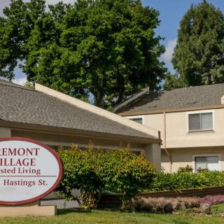 An image of a residential building with a sign for 'Fremont Village Assisted Living' surrounded by trees.