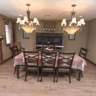 A cozy dining room with a large wooden table, surrounded by chairs and illuminated by elegant chandeliers.