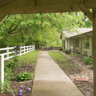 A peaceful garden pathway leading to a house, bordered by a white fence and lush greenery.