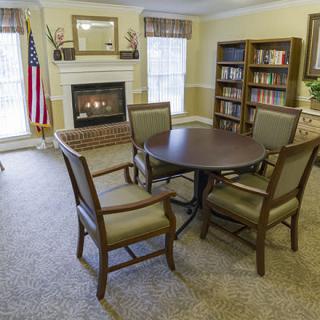 A cozy living room with a fireplace, round table and chairs, and a bookshelf by the window.