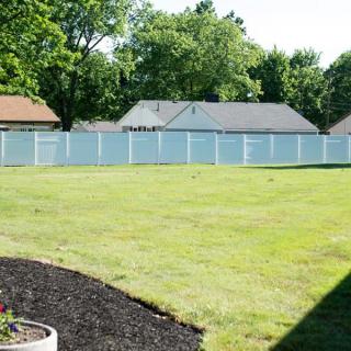 A spacious backyard with a white fence, surrounded by houses and trees.