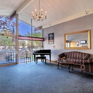 A spacious room with a piano, sofa, chandelier, and large windows letting in natural light.