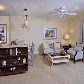 A cozy living room with a sofa, coffee table, and bookshelf, decorated with artwork and a lamp.