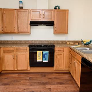 A modern kitchen with wooden cabinets and flooring, featuring a black stove and sink.