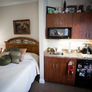 A cozy studio apartment with a bed and a small kitchenette featuring a microwave and mini-fridge.