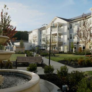A serene view of a modern apartment complex featuring landscaped gardens and a decorative fountain.