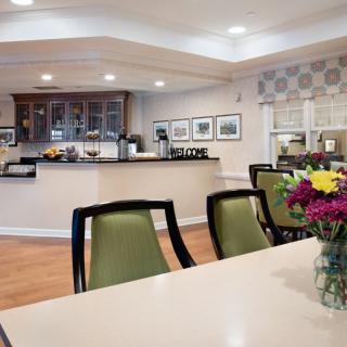 A modern dining area with a kitchenette, featuring green chairs and a table with a flower arrangement.
